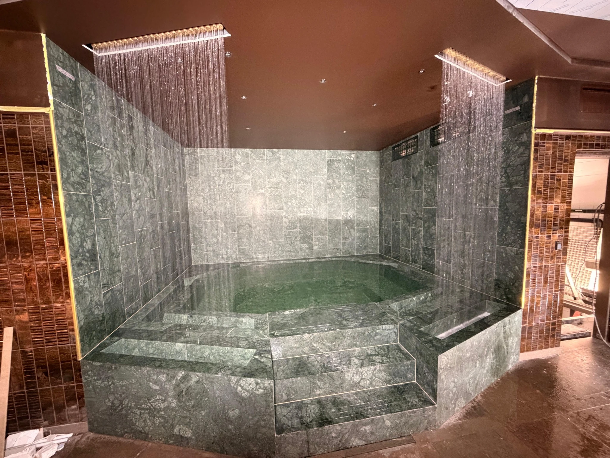 A Poolworks indoor spa with twin waterfalls flowing into a stone-lined pool